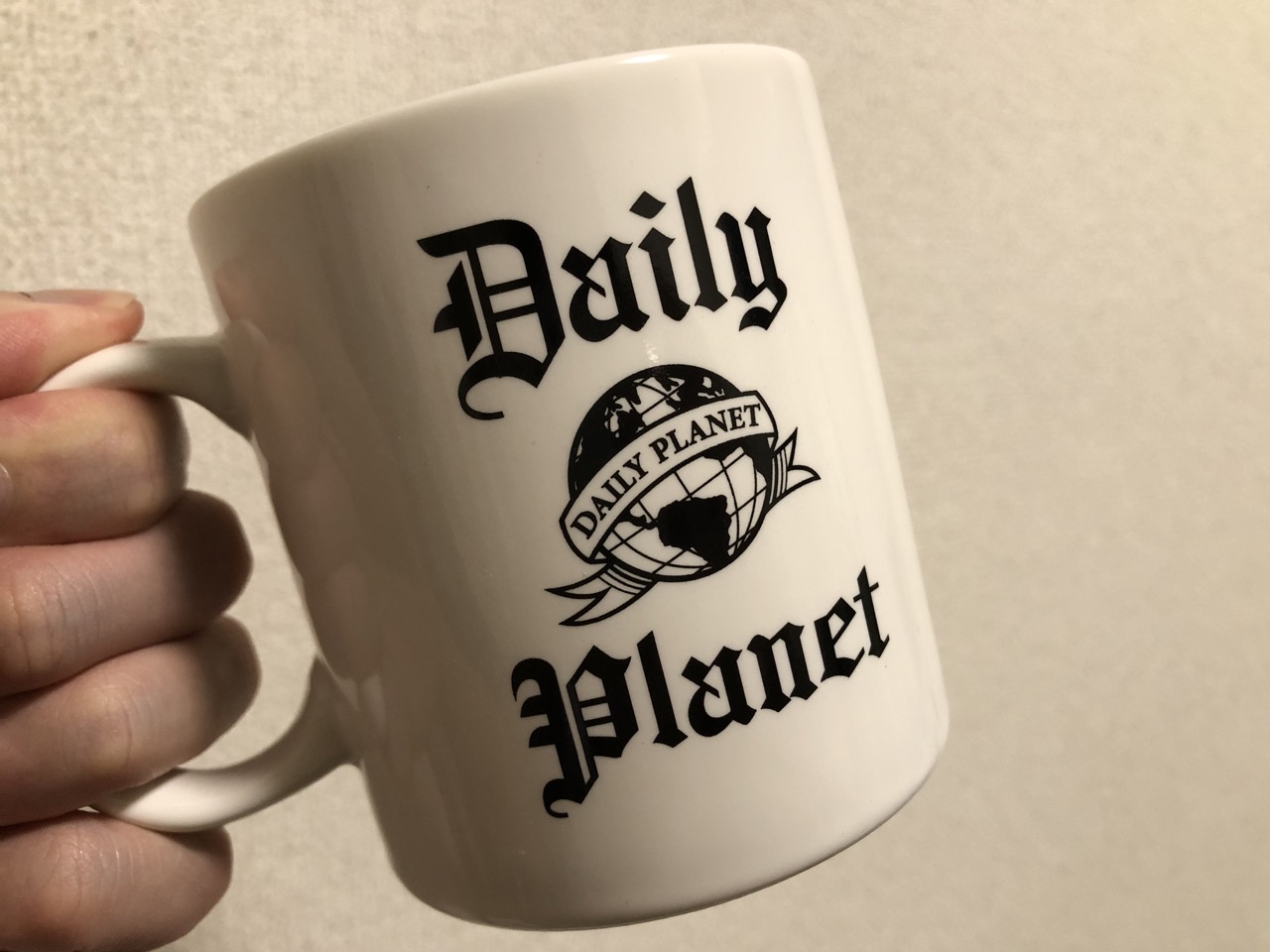 デイリー・プラネットのマグカップ。黒くて古い新聞風の字でDAILY PLANETの文字とロゴ。