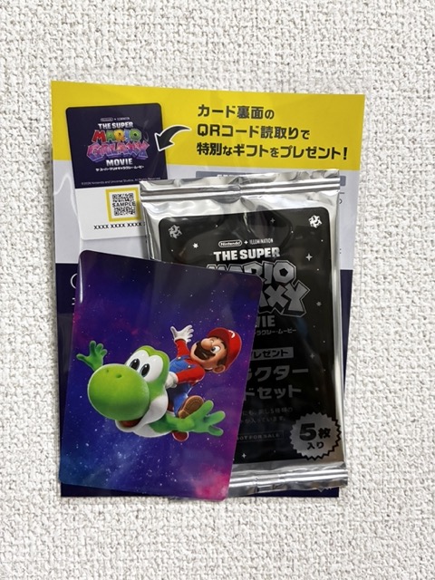 入場特典の写真。マリオがヨッシーに乗って宇宙を飛んでいるカードと銀のシュリンクに包まれたキャラクターカードセット