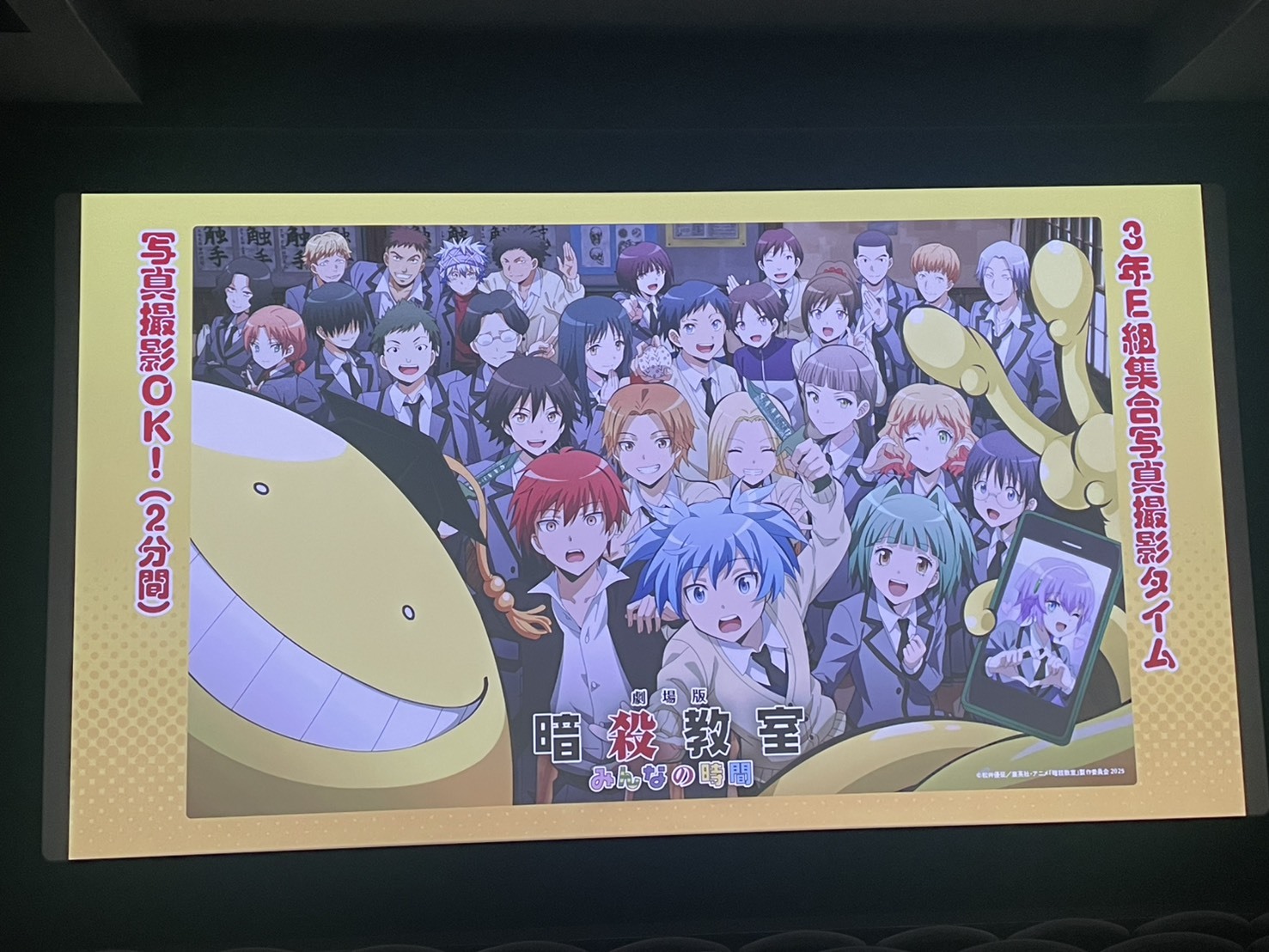 スクリーンにキャラクター達の集合写真風イラストが写っている