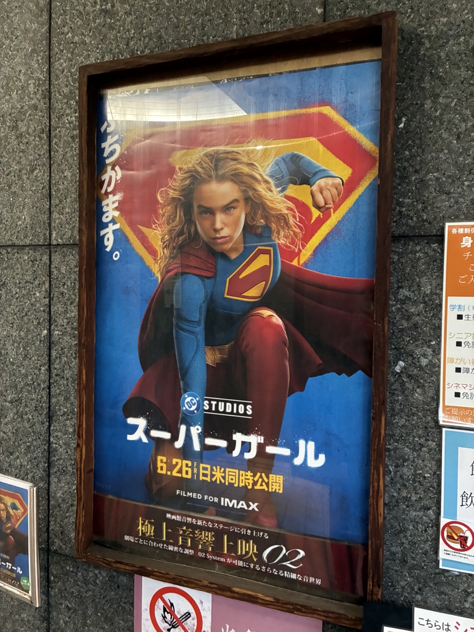 スーパーガールのポスターが壁に掲示されている。スーパーヒーロー着地を決めているスーパーガールと「ぶちかます。」のキャッチコピー