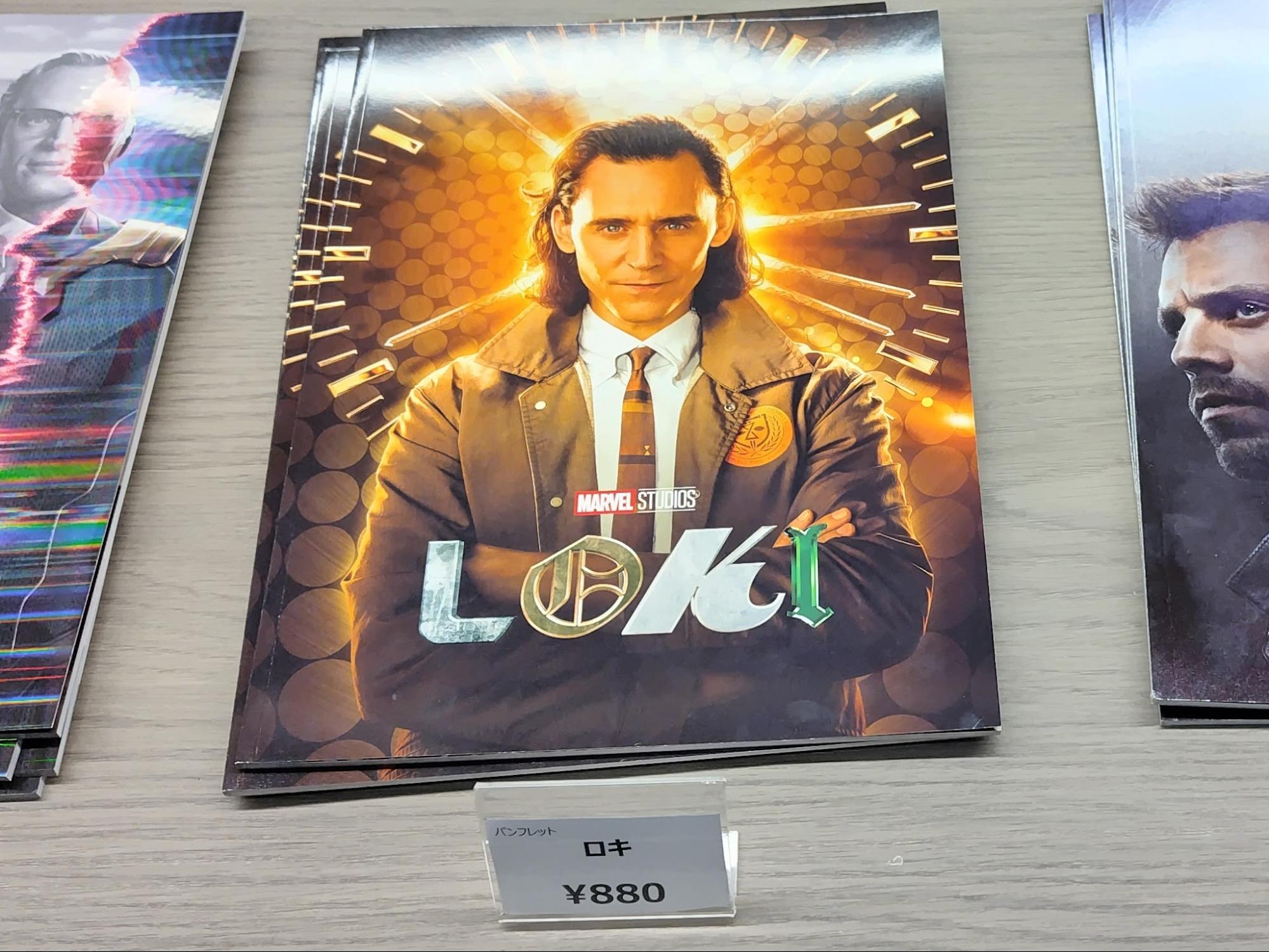 マーベル・スタジオのドラマ『ロキ』のパンフレット。ロキが腕を組んで立ち、背景に時計を思わせる金色の光が広がっている